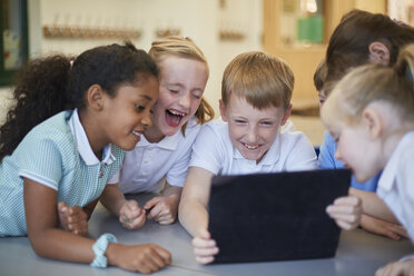 Schüler und Schülerinnen lachen über ein digitales Tablet im Klassenzimmer einer Grundschule - CUF03076