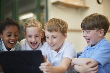 Schüler und Schülerinnen lachen über ein digitales Tablet im Klassenzimmer einer Grundschule - CUF03078