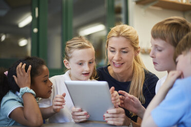 Lehrerin mit Schülern und Mädchen, die ein digitales Tablet im Klassenzimmer einer Grundschule betrachten - CUF03079