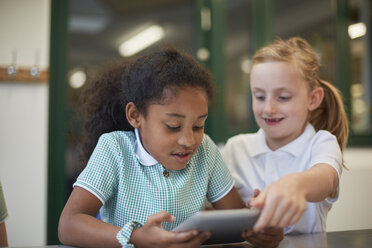 Zwei Schülerinnen betrachten ein digitales Tablet im Klassenzimmer einer Grundschule - CUF03080