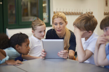 Lehrerin mit Schülerinnen und Schülern, die ein digitales Tablet im Klassenzimmer einer Grundschule betrachten - CUF03081