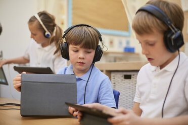 Schoolboys and girl listening to headphones in class at primary school - CUF03084