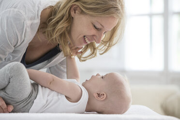 Baby boy lying on bed face to face with mother - CUF03115