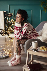 Junge Frau sitzt zu Hause, trägt Weihnachtspulli, nachdenklicher Ausdruck - CUF03121