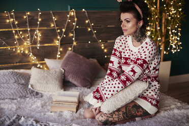 Junge Frau auf dem Bett sitzend, mit Weihnachtspulli, nachdenklicher Gesichtsausdruck - CUF03124