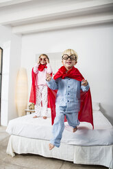 Junge und weiblicher Zwilling in roten Umhängen springen vom Bett - CUF03171