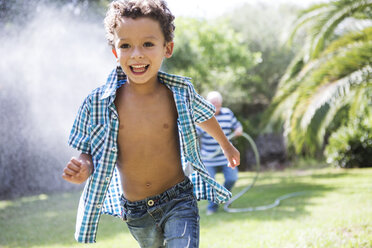 Boy running away from grandfather spraying hosepipe in garden - CUF03173