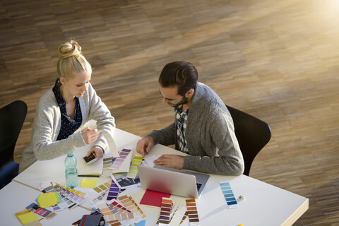 Ein Designer und eine Designerin besprechen Farbmuster auf einem Tisch im Designstudio, lizenzfreies Stockfoto