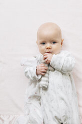 Baby girl lying on back holding soft toy looking at camera - CUF03292