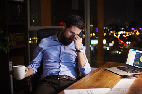 Müder junger Geschäftsmann am nächtlichen Bürotisch, lizenzfreies Stockfoto