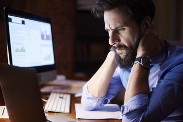 Stressed young businessman looking at laptop on office desk at night - CUF03311