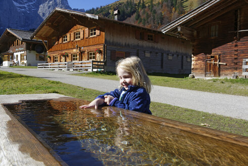Österreich, Tirol, Eng, kleines Mädchen badet Hand in der Tränke - LHF00564