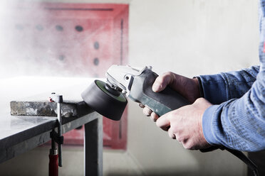 Steinmetz bei der Bearbeitung von Stein mit einer Schleifmaschine in seiner Werkstatt - CVF00456
