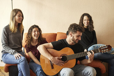 Glückliche Freunde hören einem Mann zu, der auf der Couch Gitarre spielt - JRFF01625