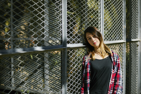 Portrait of beautiful young woman leaning against a fence stock photo