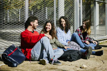 Four happy friends sitting at fence talking - JRFF01631