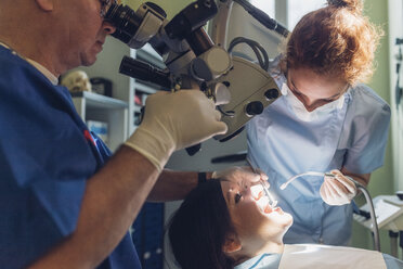 Zahnarzt und Zahnarzthelferin führen einen zahnärztlichen Eingriff an einer Patientin durch - CUF03453