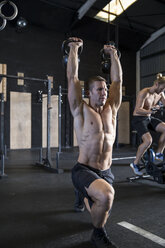 Two men exercising in gymnasium, using kettlebells and air resistance exercise bike - CUF03489