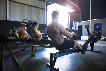 Gruppe von Menschen, die in einer Sporthalle an Rudergeräten trainieren, Rückansicht - CUF03496