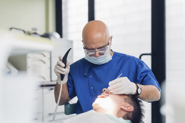 Zahnarzt bei der Durchführung eines zahnärztlichen Eingriffs an einem männlichen Patienten - CUF03519