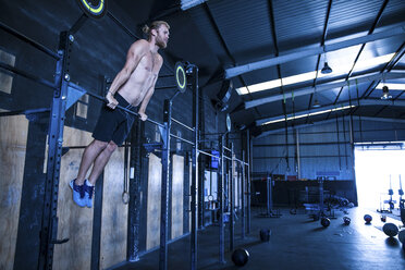 Man exercising in gymnasium, using pull up bars - CUF03541