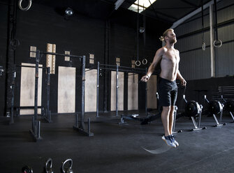Mann trainiert in einer Turnhalle, springt mit einem Springseil - CUF03545
