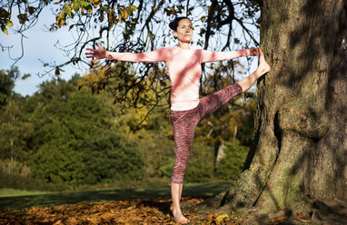 Woman doing yoga in park on autumn day - CUF03600