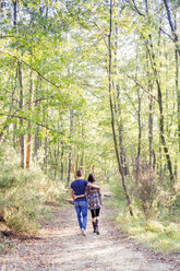Rückansicht eines Paares, das auf einem von Bäumen gesäumten Weg spazieren geht - CUF03702