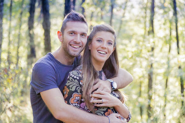 Couple in forest hugging looking at camera smiling - CUF03703