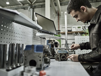 Worker in metalworking factory measuring cylinder head with caliper - CVF00468