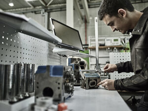 Arbeiter in einem metallverarbeitenden Betrieb, der einen Zylinderkopf mit einem Messschieber misst - CVF00468