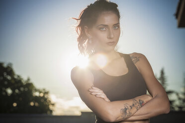 Portrait of young woman with tattoos, arms folded, outdoors - CUF03749