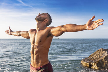 Young man standing by sea, arms outstretched, Fortaleza, Ceara, Brazil - CUF03770