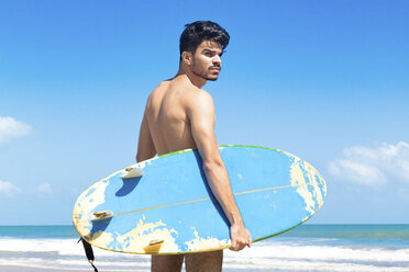 Junger Mann steht am Strand und hält ein Surfbrett, Fortaleza, Ceara, Brasilien - CUF03773