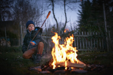 Junge röstet in der Abenddämmerung Marshmallows am Lagerfeuer im Garten - CUF03837