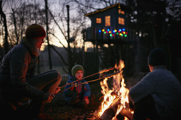 Mature woman and two sons toasting marshmallows on campfire at night - CUF03839