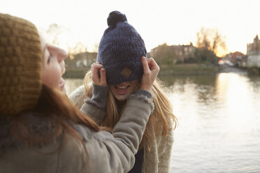Junge Frau setzt einer Freundin eine Strickmütze auf, die Mütze verdeckt die Augen, lachend - CUF03936