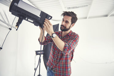 Männlicher Fotograf bei der Vorbereitung der Beleuchtungsausrüstung für ein Fotoshooting im Studio - CUF03953