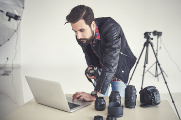 Männlicher Fotograf, der ein Studio-Foto-Shooting am Laptop überprüft - CUF03957
