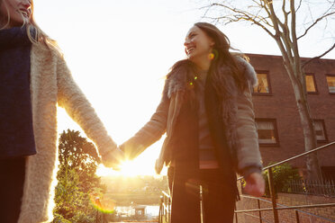 Two female friends outdoors, walking hand in hand, laughing - CUF04002