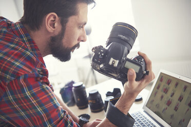 Male photographer reviewing photo shoot on laptop in studio - CUF04009