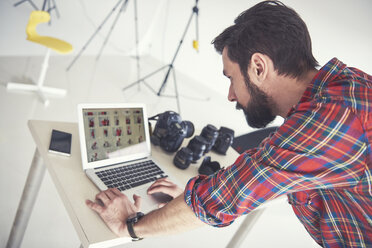 Männlicher Fotograf, der eine Fotoaufnahme am Laptop im Studio überprüft - CUF04012