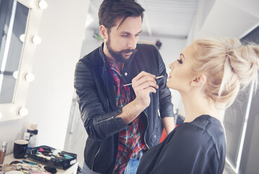 Männlicher Make-up-Künstler trägt Lippenstift auf ein Modell für ein Fotoshooting auf - CUF04023