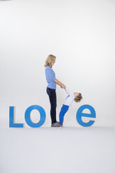 Mutter und Sohn halten sich an den Händen, stehen zwischen dreidimensionalen Buchstaben und bilden das Wort LOVE - CUF04067