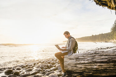 Mann sitzt mit Laptop am Strand im Juan de Fuca Provincial Park, Vancouver Island, British Columbia, Kanada - CUF04080