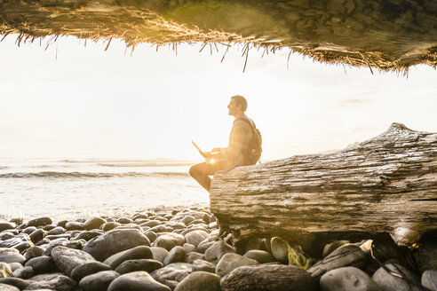 Mann sitzt mit Laptop und schaut vom Strand im Juan de Fuca Provincial Park, Vancouver Island, British Columbia, Kanada, hinaus - CUF04085