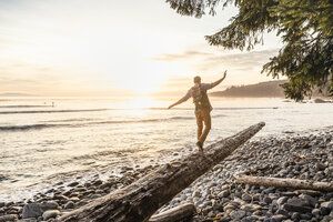 Mann balanciert auf einem Treibholzstamm am Strand im Juan de Fuca Provincial Park, Vancouver Island, British Columbia, Kanada - CUF04086