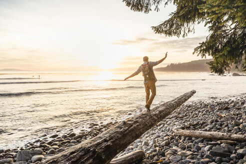 Man balancing on driftwood log on beach in Juan de Fuca Provincial Park, Vancouver Island, British Columbia, Canada - CUF04086