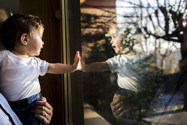 Kleiner Junge in den Armen seines Vaters, der durch das Fenster schaut und es berührt - CUF04139