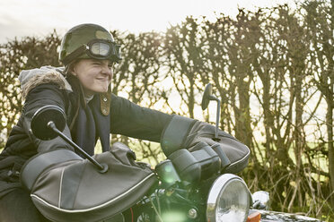 Junge verzieht das Gesicht, während er auf einem Motorrad am Straßenrand sitzt - CUF04152